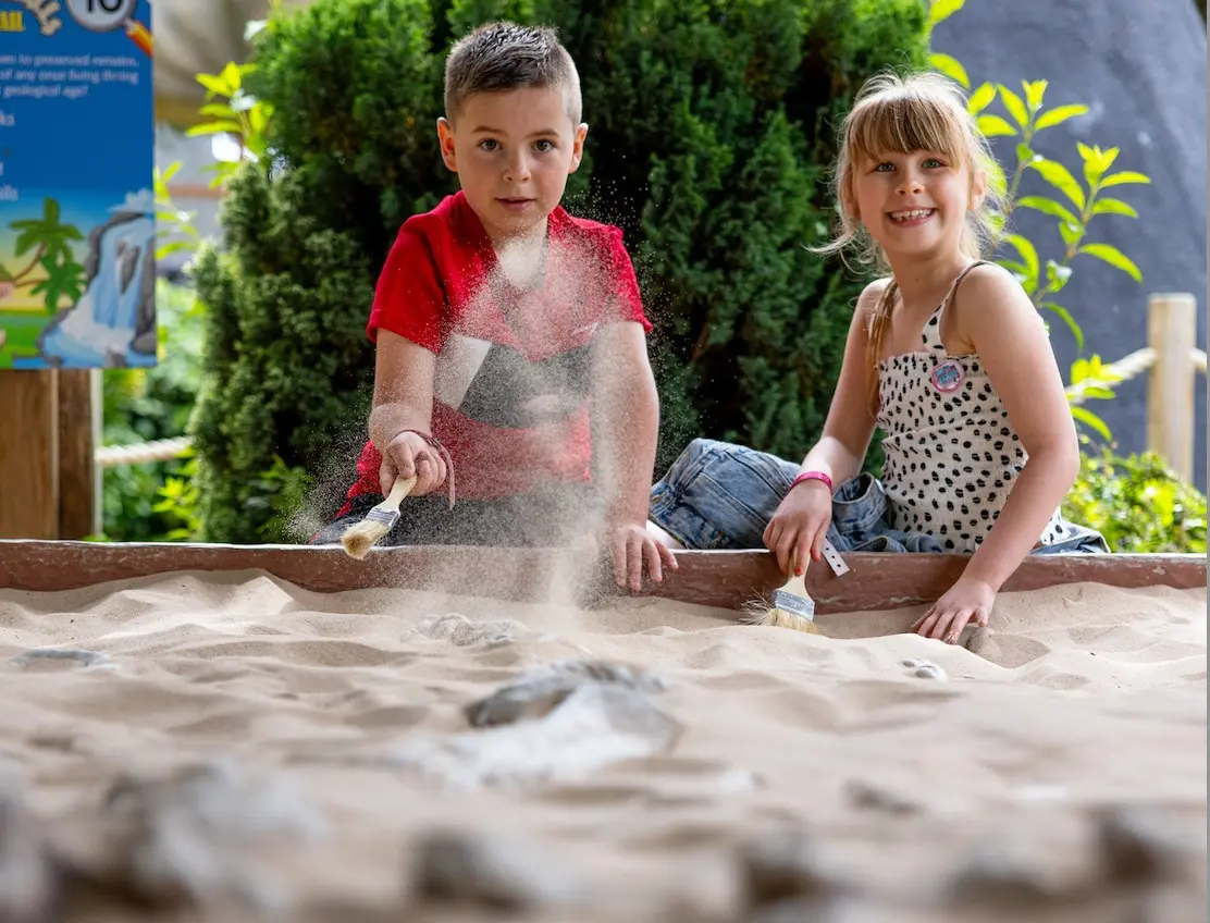 Two children brushing sand away at the fossil dig