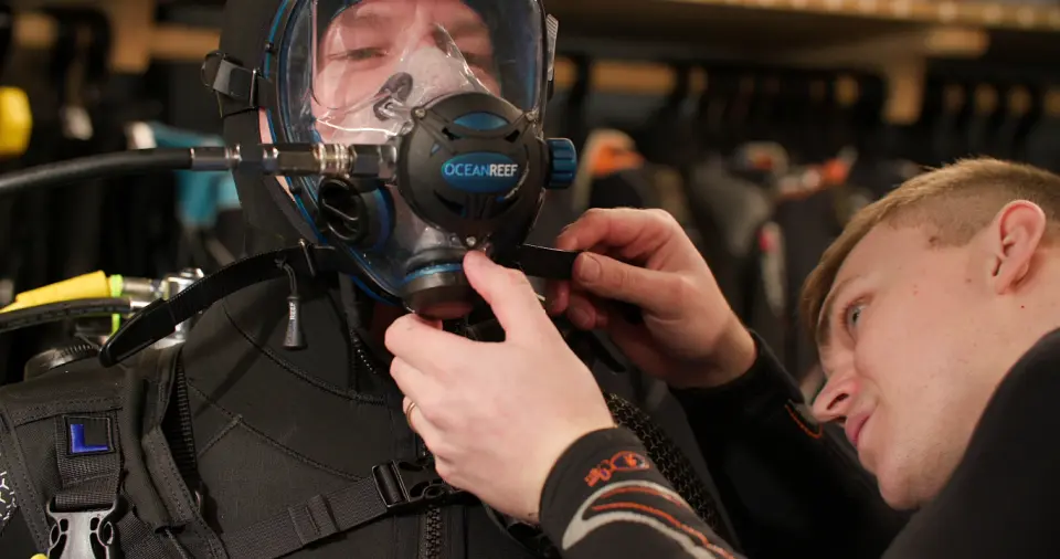 A member of the dive team adjusting a customer’s full-face mask before a dive